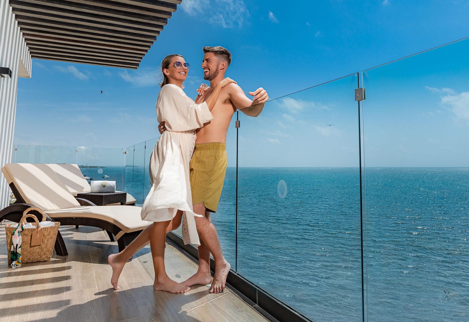hombre y mujer abrazados y riendo, en el balcon de una suite frente al mar en el hotel Sensira en Riviera Maya