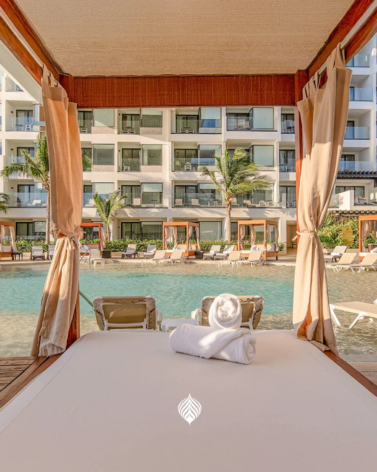 Vista desde cabaña junto a alberca en resort tropical, con cortinas y ambiente relajante.