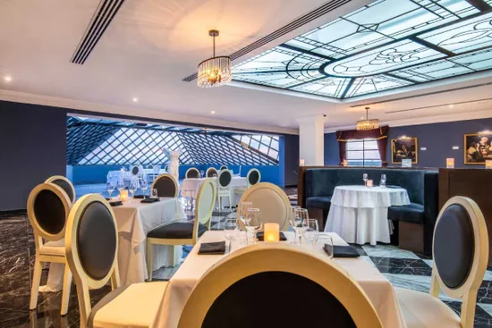 Interior elegante de restaurante con mesas vestidas, sillas modernas y techo decorativo iluminado.