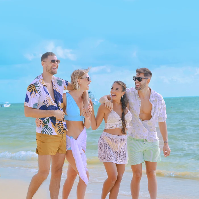 Grupo de amigos jóvenes sonriendo y caminando por la orilla de la playa.