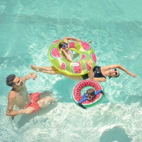 Familia relajándose en la piscina con flotadores de sandía durante vacaciones.